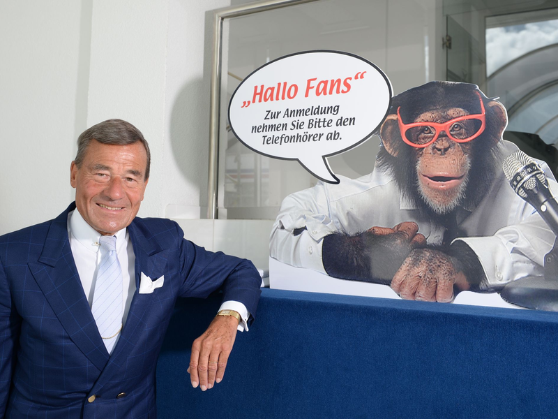 Wolfgang Grupp senior mit einem Werbeschild, auf dem der bekannte Werbe-Affe Charly abgebildet ist. - Foto: picture alliance / Patrick Seeger/dpa
