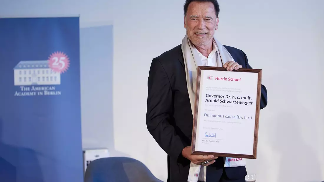 Arnold Schwarzenegger bekommt von Cornelia Woll und Robert Habeck die Ehrendoktorwürde überreicht. - Bild: Joerg Carstensen/dpa