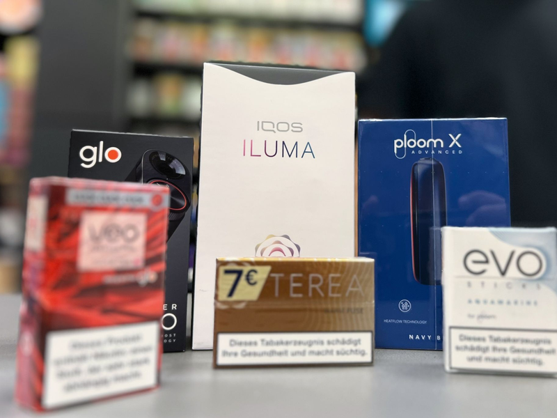 Die Tabakerhitzer-Elektrogeräte der Marken Glo von British American Tobacco (BAT), Iqos von Philip Morris und Ploom von Japan Tobacco International (JTI) mit den dazugehörigen Tabakstick-Marken liegen auf der Verkaufstheke eines Geschäfts. - Foto: Wolf von Dewitz/dpa