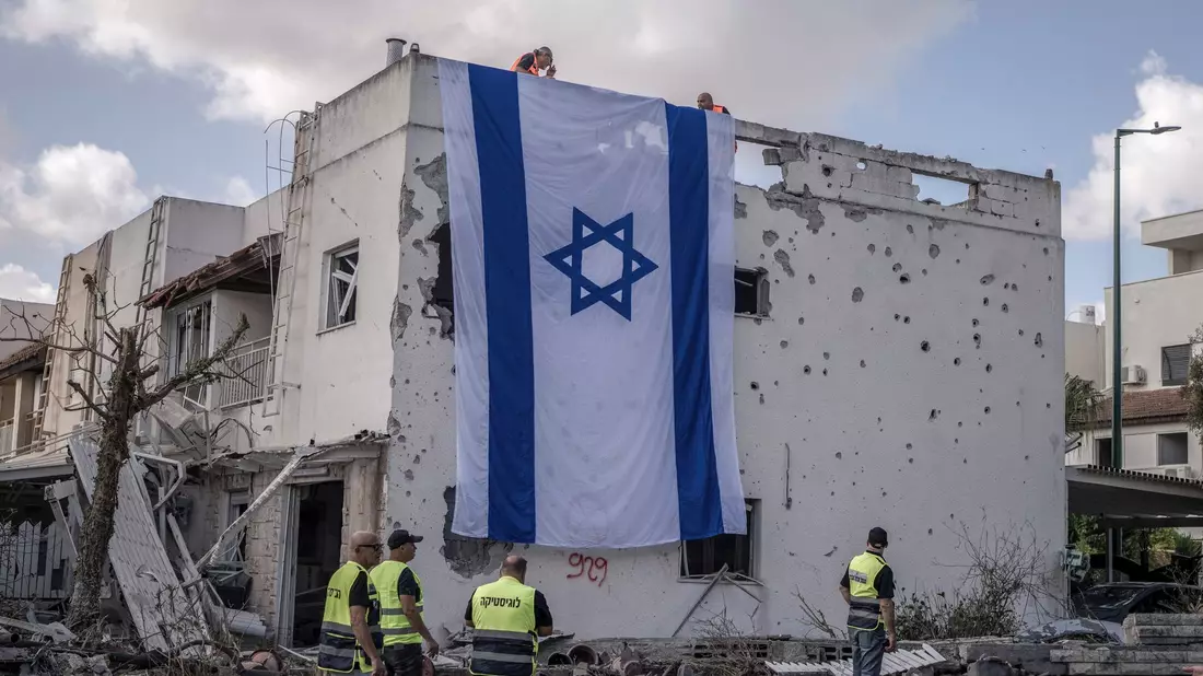 Eine riesige israelische Fahne hängt vom Dach eines beschädigten Gebäudes in Kiriat Bialik. - Bild: Ilia Yefimovich/dpa