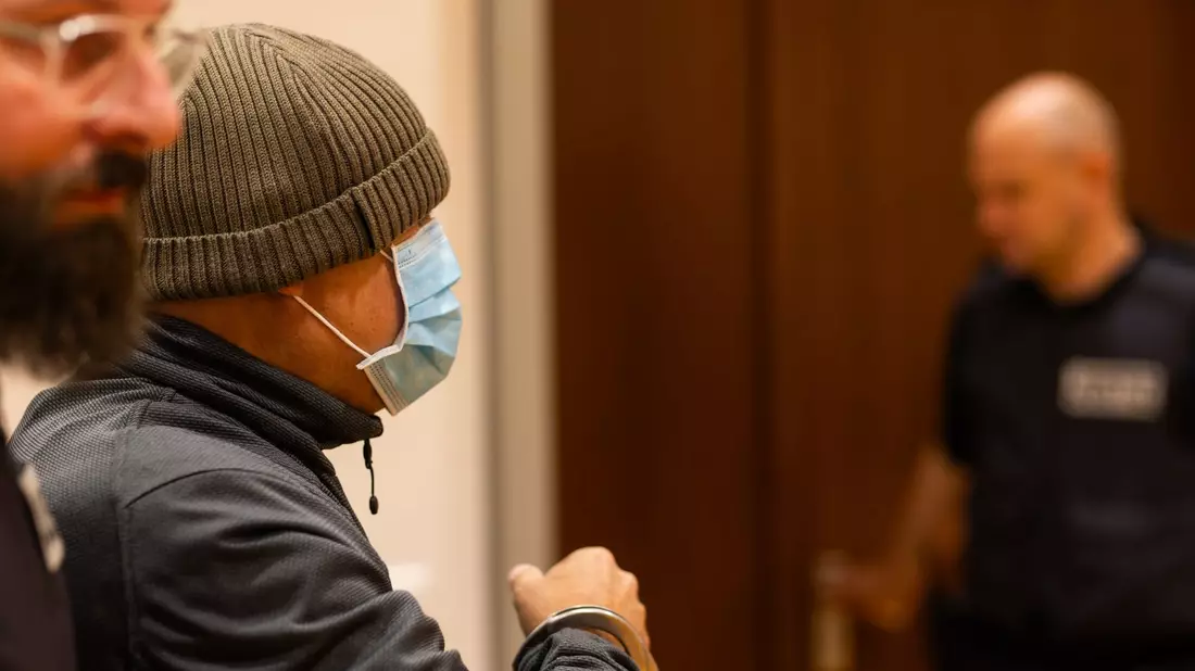 Ein Justizbeamter nimmt dem Angeklagten (links) im Gerichtssaal die Handschellen ab, während dessen Verteidiger daneben steht. - Bild: Philipp von Ditfurth/dpa