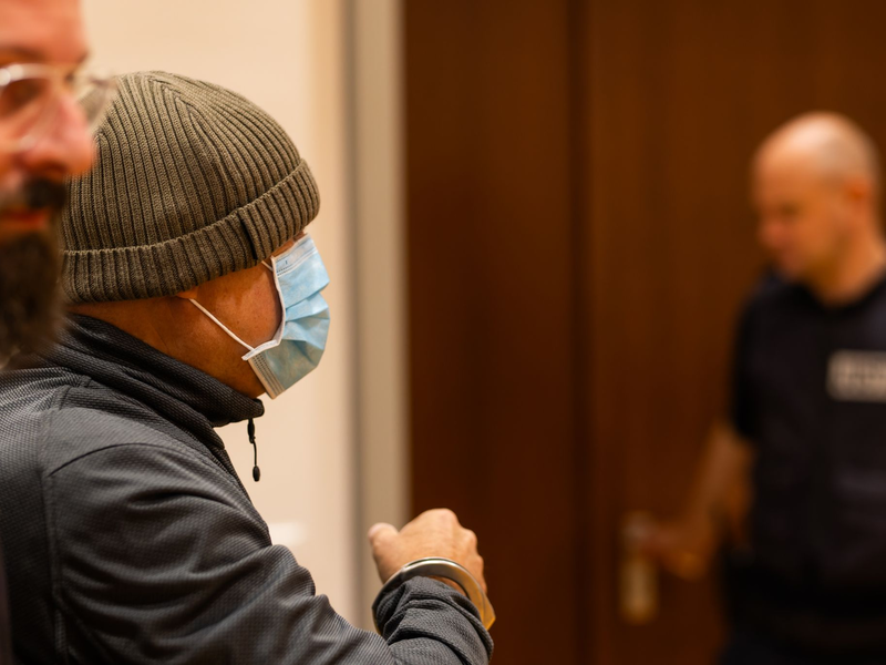 Ein Justizbeamter nimmt dem Angeklagten (links) im Gerichtssaal die Handschellen ab, während dessen Verteidiger daneben steht. - Foto: Philipp von Ditfurth/dpa