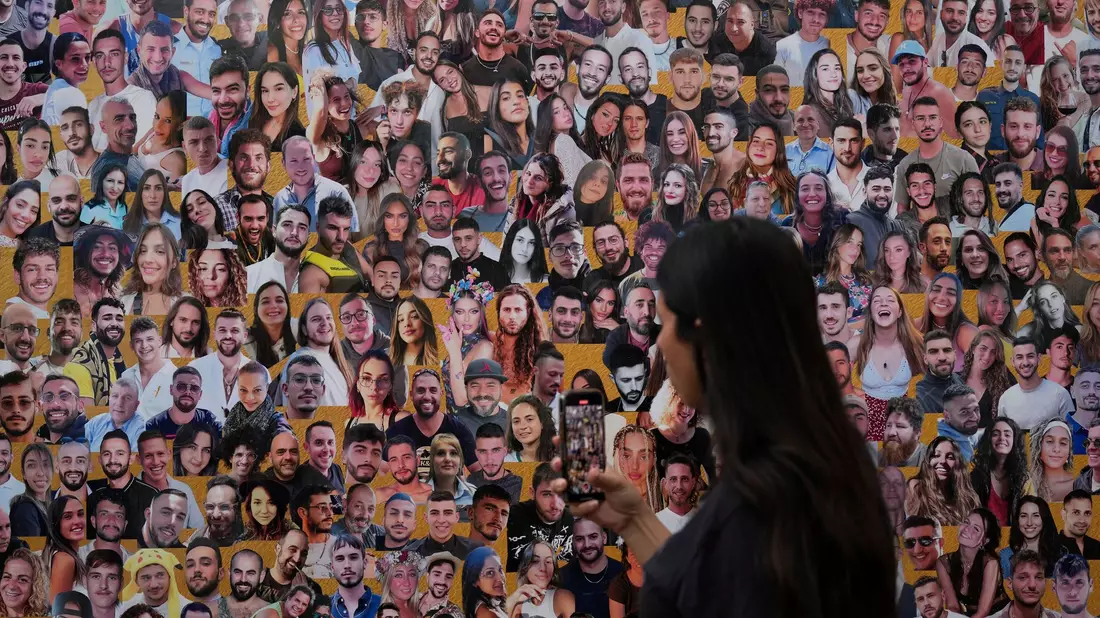 Eine Frau fotografiert eine Wand mit Porträts der Opfer am Ort des Nova-Musikfestivals. (Archivbild) - Bild: Ariel Schalit/AP/dpa