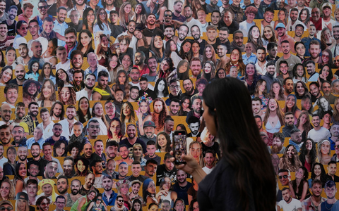 Eine Frau fotografiert eine Wand mit Porträts der Opfer am Ort des Nova-Musikfestivals. (Archivbild) - Foto: Ariel Schalit/AP/dpa