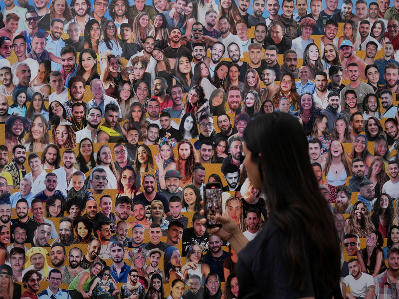 Eine Frau fotografiert eine Wand mit Porträts der Opfer am Ort des Nova-Musikfestivals. (Archivbild) - Foto: Ariel Schalit/AP/dpa