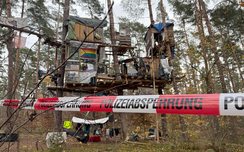 PolizeikrĂ€fte sichern das Waldgebiet hinter einer Absperrung. Umweltaktivisten, die gegen Tesla protestieren, mĂŒssen ihr Camp rĂ€umen. - Foto: Lutz Deckwerth/dpa PolizeikrĂ€fte sichern das Waldgebiet hinter einer Absperrung. Umweltaktivisten, die gegen Tesla protestieren, mĂŒssen ihr Camp rĂ€umen. - Foto: Lutz Deckwerth/dpa
