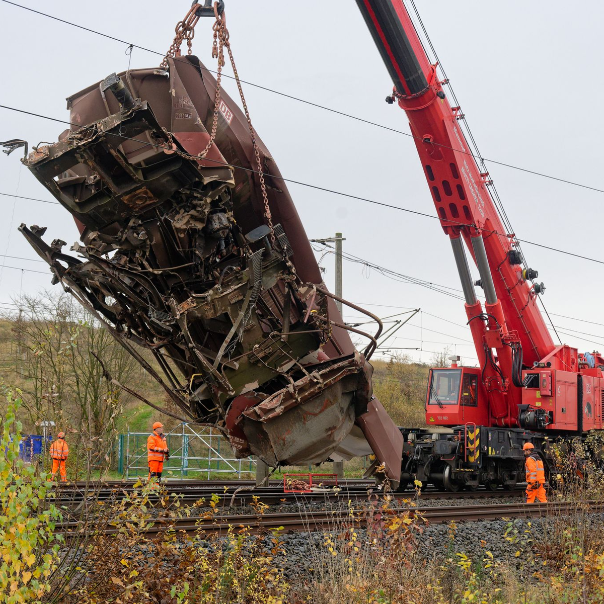 Arbeiter befestigen den demolierten Güterwaggon an einem Kran. - Foto: Henning Kaiser/dpa