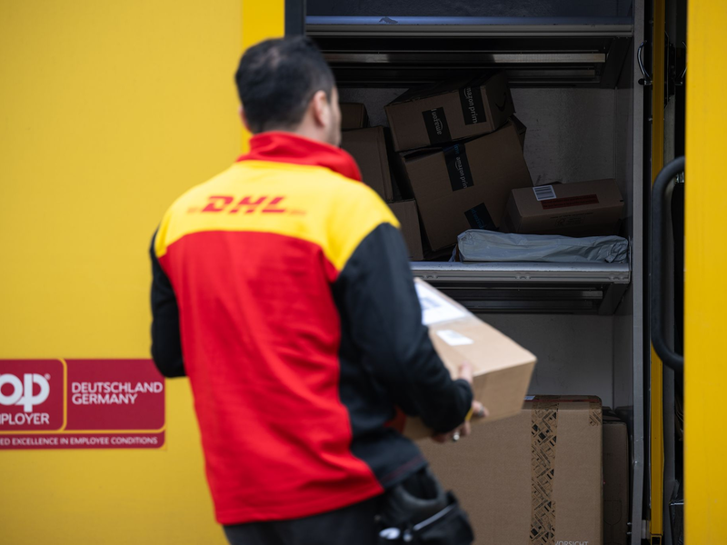 Ein Post-Mitarbeiter trägt ein Paket in einen Lieferwagen. - Foto: Hannes P. Albert/dpa