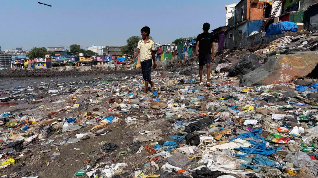 Menschen spazieren am Strand des Badhwar Park im indischen Mumbai an Plastikmüll vorbei. (Archivbild) - Bild: Rajanish Kakade/AP/dpa