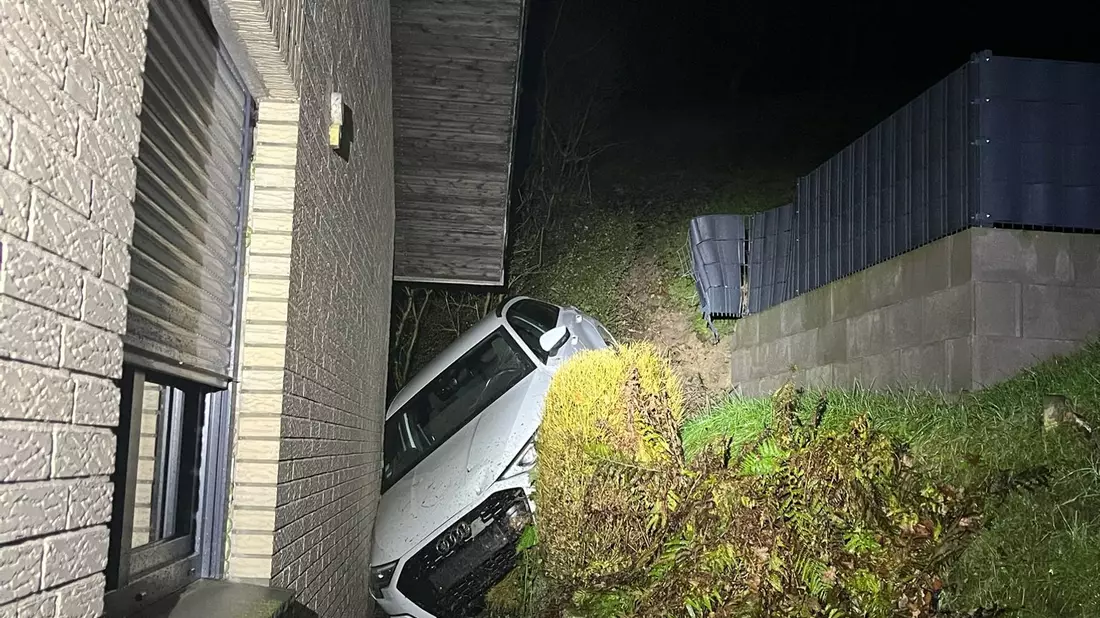 Das Auto steckt zwischen einem Abhang und dem verklinkerten Wohnhaus fest. - Bild: -/Kreispolizei Paderborn/dpa