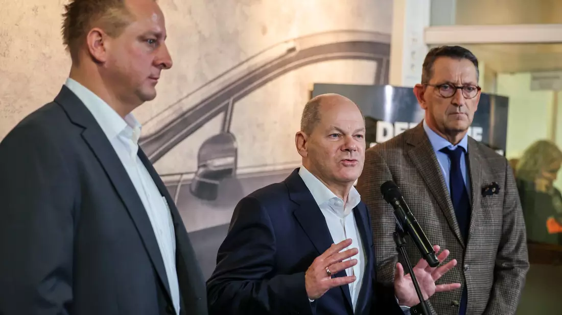 Betriebsratschef Benjamin Gruschka (l) neben Bundeskanzler Olaf Scholz (SPD) und Marcus Wassenberg (r), Geschäftsführer der Ford-Werke. - Bild: Christoph Reichwein/dpa