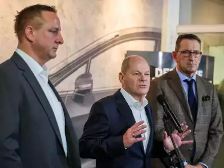 Betriebsratschef Benjamin Gruschka (l) neben Bundeskanzler Olaf Scholz (SPD) und Marcus Wassenberg (r), Geschäftsführer der Ford-Werke. - Foto: Christoph Reichwein/dpa