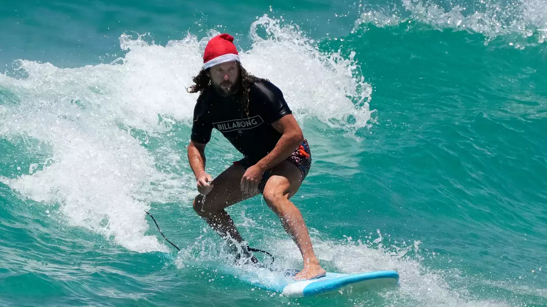 Surfende Santas gehören in Australien zu Weihnachten dazu. (Archivbild) - Bild: Rick Rycroft/AP/dpa
