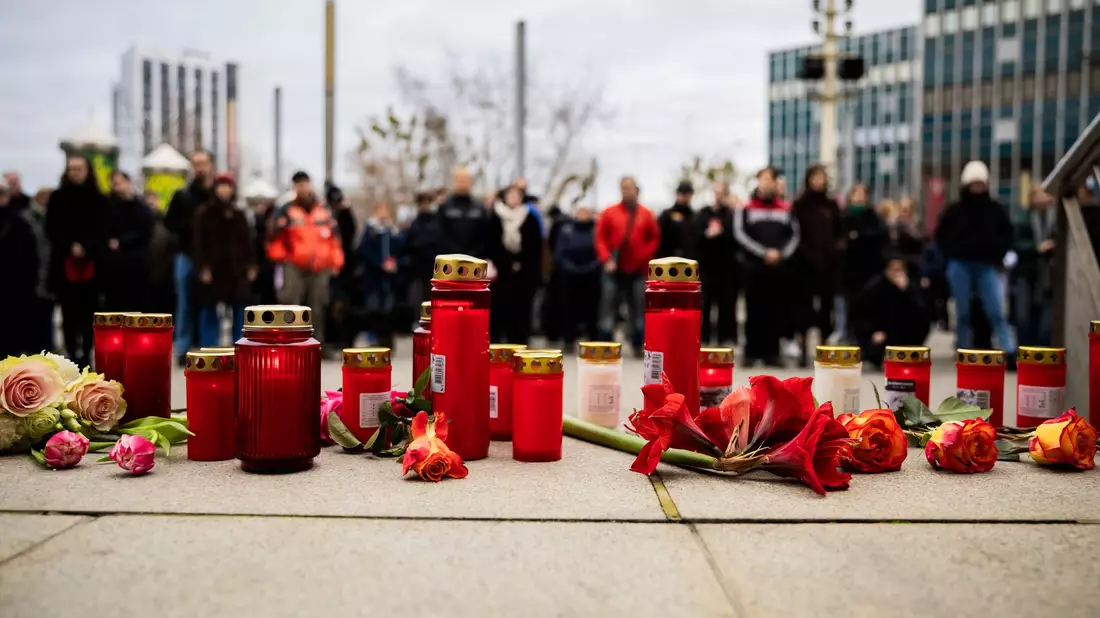 Menschen zünden Kerzen an und legen Blumen nieder. - Bild: Christoph Soeder/dpa