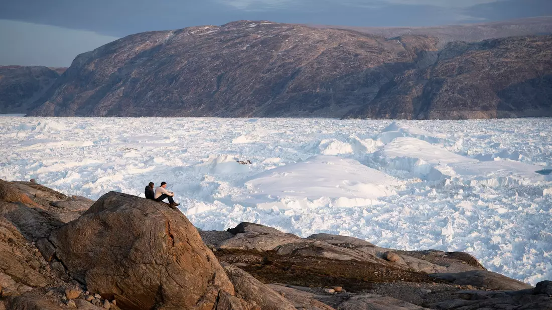 Zwei Studenten der New York University sitzen auf einem Felsen mit Blick auf den grönländischen Helheim-Gletscher.  - Bild: Felipe Dana/AP/dpa