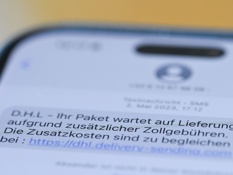 Auf einem Smartphone ist eine Betrugs-SMS zu lesen, in der Kriminelle ein Paket ankündigen und dafür Zollgebühren einfordern.  - Foto: Wolf von Dewitz/dpa