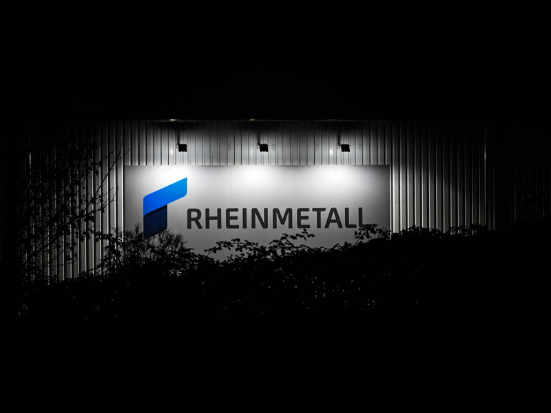 Das beleuchtete Logo und der Schriftzug der Rüstungsfirma Rheinmetall hängt an einer Produktionshalle. - Foto: Lars Penning/dpa