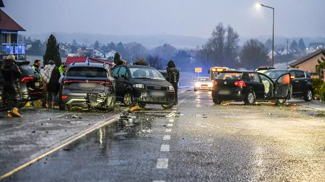 Nach einem Unfall bei Glatteis mit mehreren Fahrzeugen in Baden-Württemberg stehen Helfer und Beteiligte an den Autos auf einer Straße.  - Bild: Jason Tschepljakow/dpa