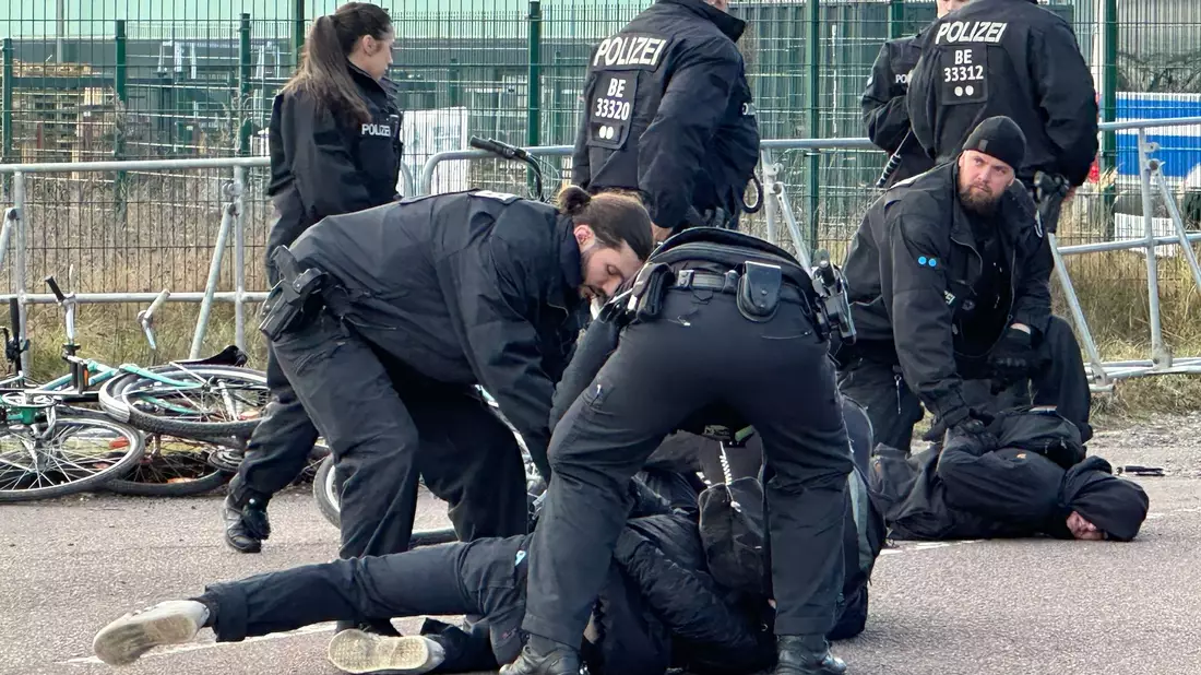 Polizisten halten Demonstranten am Boden fest. Sie hatten zuvor versucht mit Fahrrädern Richtung Veranstaltungshalle vorzudringen. - Bild: Jörg Ratzsch/dpa