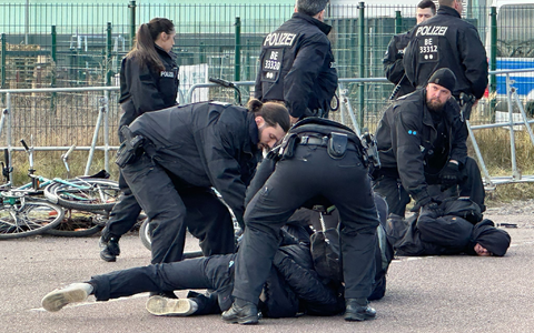 Polizisten halten Demonstranten am Boden fest. Sie hatten zuvor versucht mit Fahrrädern Richtung Veranstaltungshalle vorzudringen. - Foto: Jörg Ratzsch/dpa