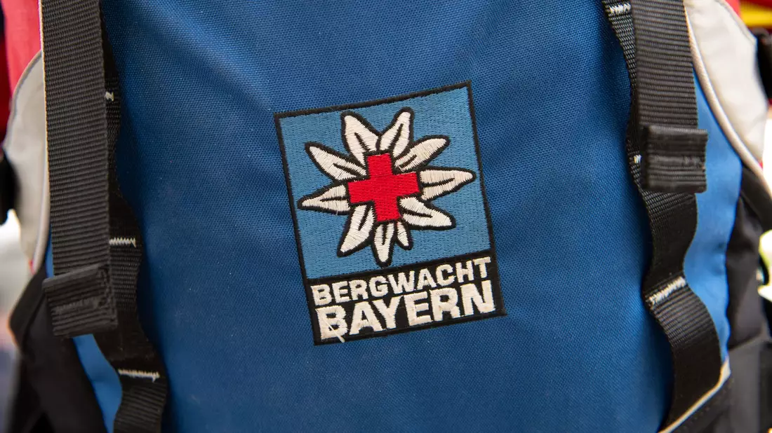 Das Logo der Bergwacht ist an einem Rucksack zu sehen. Bei Oberstdorf musste die Bergwacht nun einen Mann retten, der ohne richtige Ausrüstung und Erfahrung zwei Nächte in den Bergen verbrachte. (Archivfoto-Illustration) - Bild: Sven Hoppe/dpa