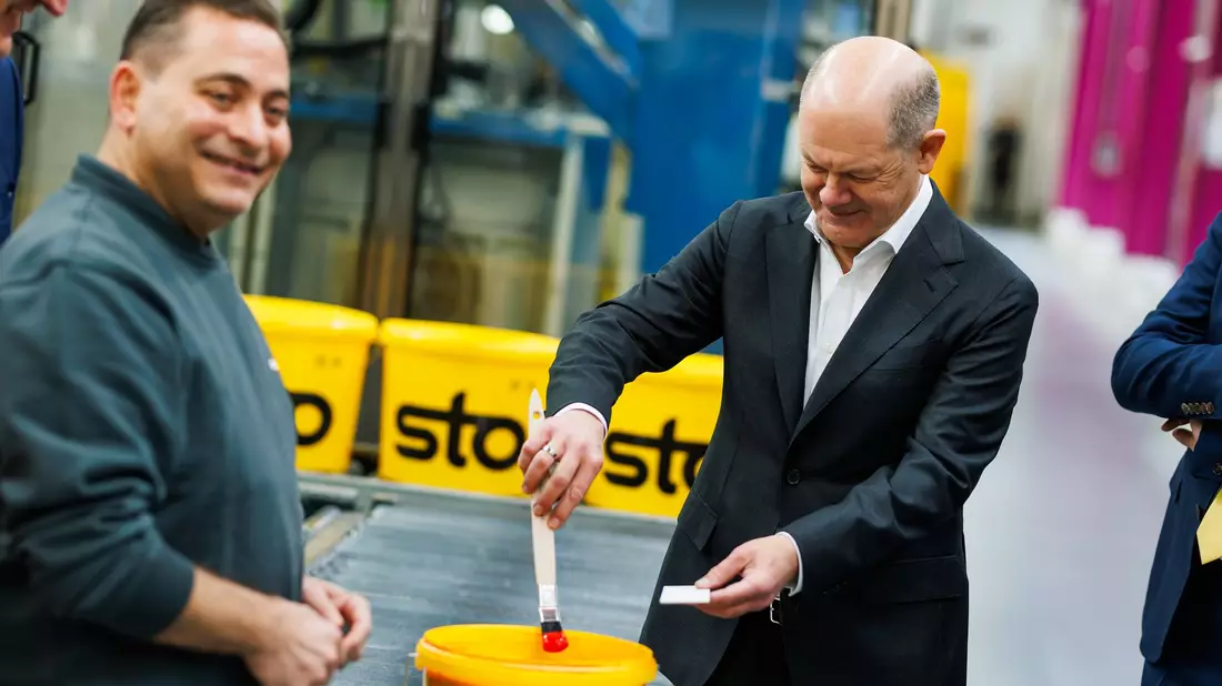 Kanzler Scholz macht beim Baustoffhersteller Sto eine Farbenprobe. - Bild: Philipp von Ditfurth/dpa