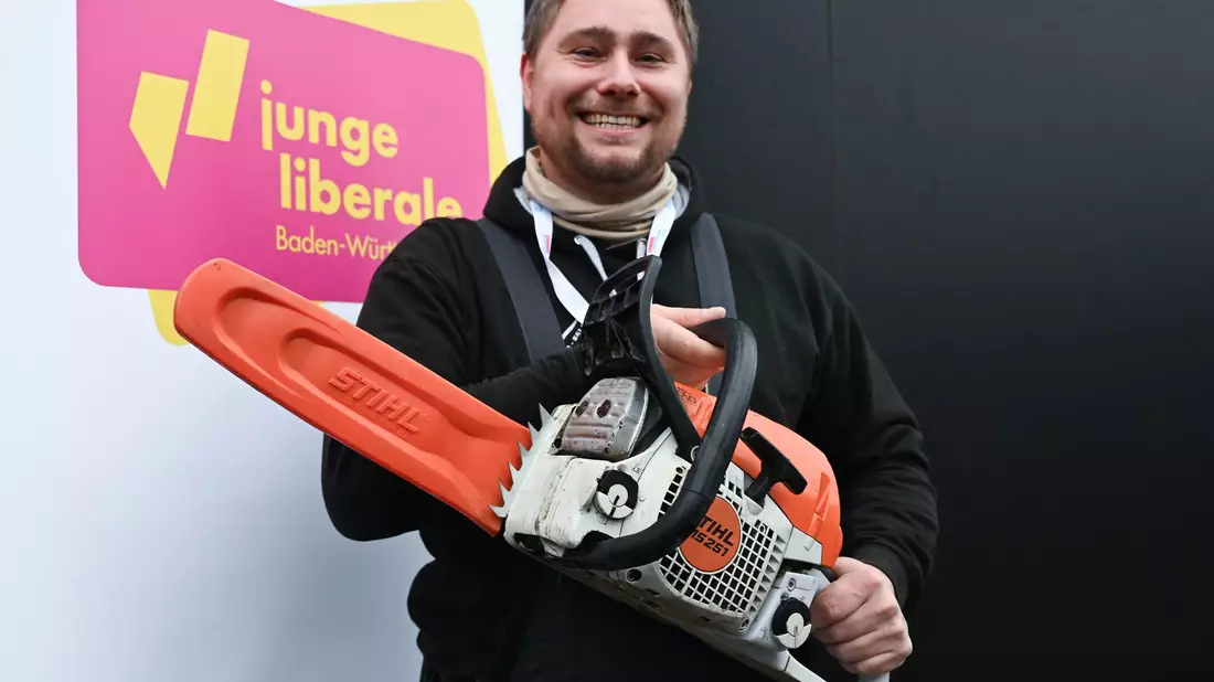 Mit der Kettensäge will Mark Hohensee, Landesvorsitzender der Jungen Liberalen, packt für den Bürokratieabbau symbolisch die Kettensäge aus.  - Bild: Bernd Weißbrod/dpa