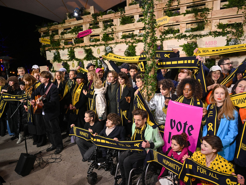 Mit Schals und Schildern haben Prominente an einer Protestaktion von SOS Humanity teilgenommen. - Foto: Christophe Gateau/dpa