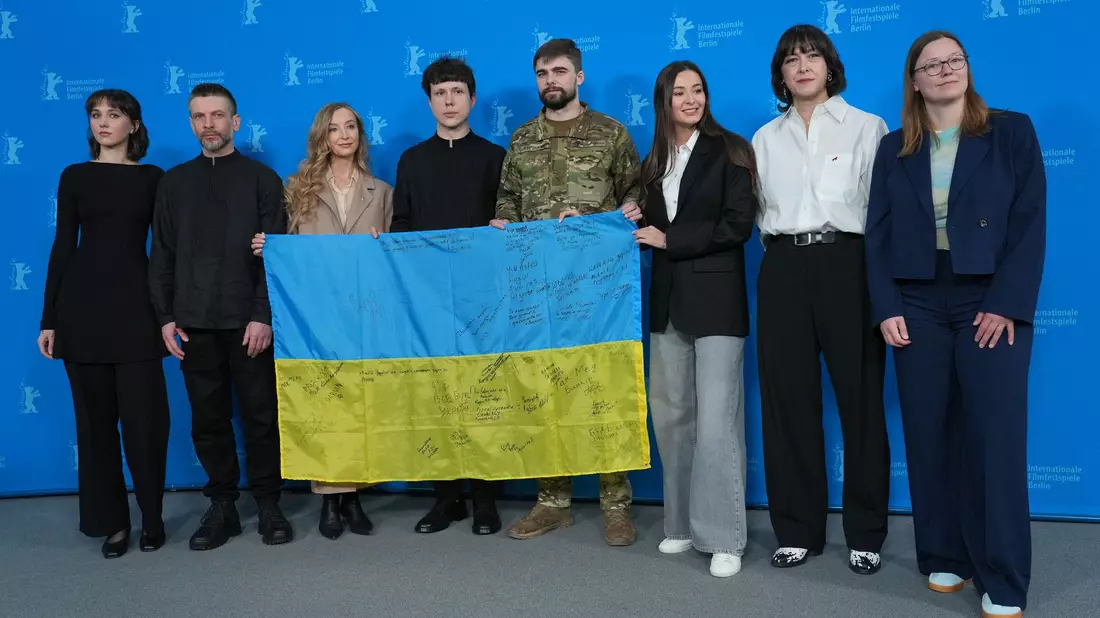 Das Team des Films «Strichka chasu» mit einer ukrainischen Flagge, auf der die Lehrerkollegen des Protagonisten und jetzigen Soldaten Borys Khovriak (M) unterschrieben haben.  - Bild: Soeren Stache/dpa