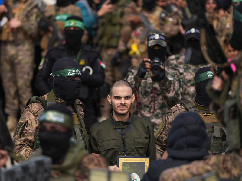 Ein vermummter Hamas-Kämpfer gibt einer israelischen Geisel Anweisungen während einer Übergabe-Veranstaltung im Gazastreifen. - Foto: Abdel Kareem Hana/AP/dpa