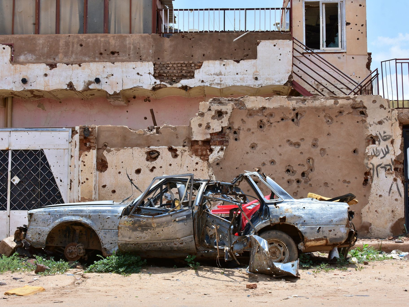 Ein zerstörtes Auto steht im sudanesischen Omdurman vor einem Haus voller Einschüsse. (Archivbild) - Foto: Mudathir Hameed/dpa