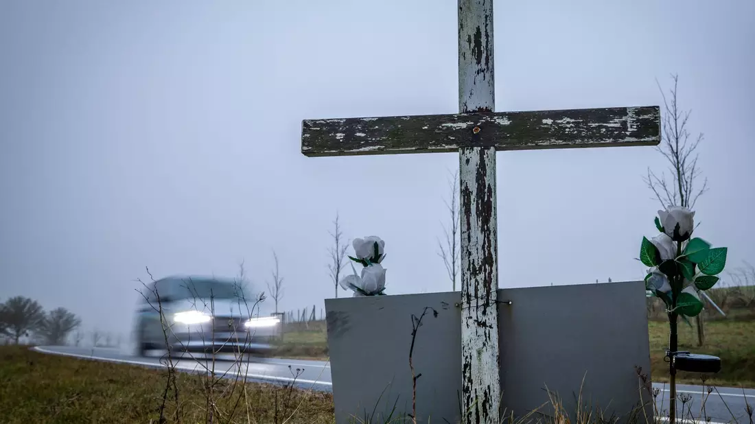 in Auto fährt auf einer Landstraße an einem hölzernen Kreuz vorbei, welches zur Erinnerung an ein Unfallopfer aufgestellt wurde. - Bild: Jens Büttner/dpa