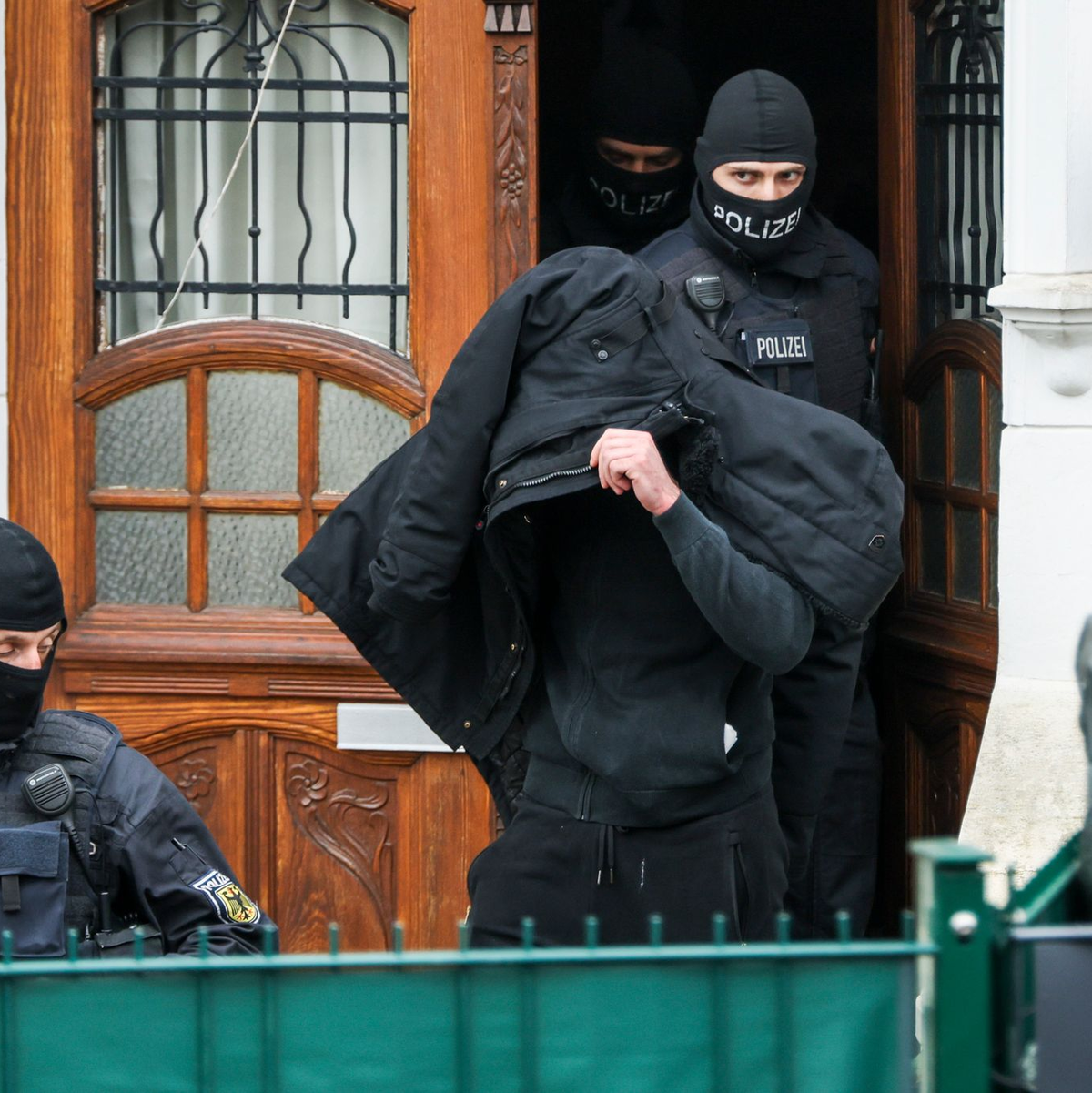 Polizeibeamte führen einen Tatverdächtigen aus einem durchsuchten Haus.  - Foto: Christoph Reichwein/dpa