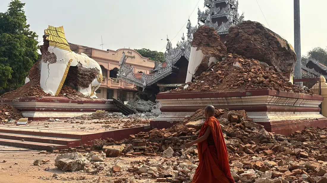 Ein buddhistischer Mönch geht in der Nähe einer eingestürzten Pagode nach einem Erdbeben in Mandalay.  - Bild: Thein Zaw/AP/dpa