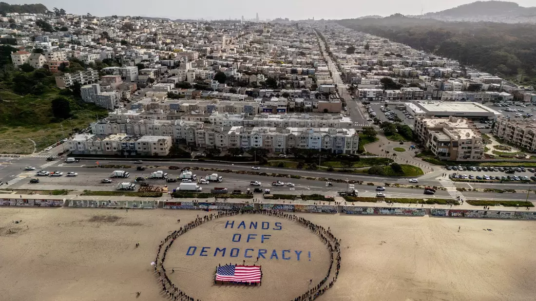An einem Strand im Bundesstaat Kalifornien bildeten Demonstranten einen menschlichen Kreis um eine US-Flagge und den Slogan «Hände weg von der Demokratie!».  - Bild: Stephen Lam/San Francisco Chronicle/AP/dpa