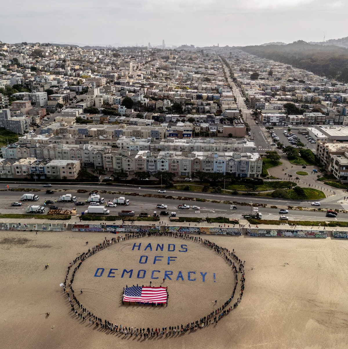 An einem Strand im Bundesstaat Kalifornien bildeten Demonstranten einen menschlichen Kreis um eine US-Flagge und den Slogan «Hände weg von der Demokratie!».  - Foto: Stephen Lam/San Francisco Chronicle/AP/dpa