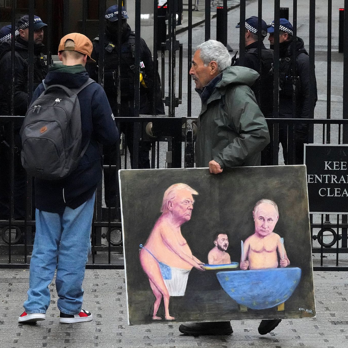 Ein Künstler geht in London mit einem Gemälde von Trump, Selenskyj und Putin am Tag der Ukraine-Gespräche vor den Toren der Downing Street 10 entlang.  - Foto: Frank Augstein/AP/dpa