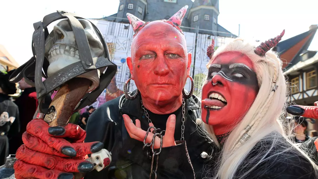 Im Teufelskostüm stehen Besucher auf dem Marktplatz in Wernigerode.  - Bild: Matthias Bein/dpa