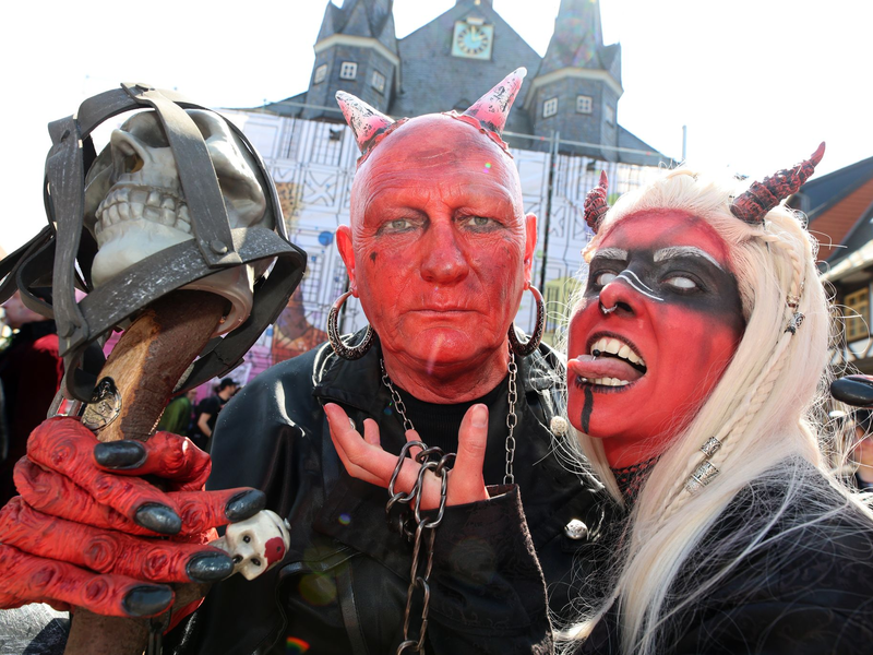 Im Teufelskostüm stehen Besucher auf dem Marktplatz in Wernigerode.  - Foto: Matthias Bein/dpa
