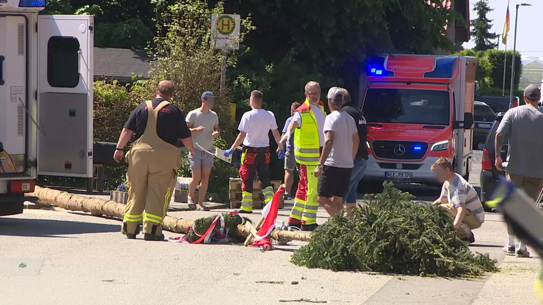 Der umgestürzte Maibaum liegt auf der Straße vor einem Einsatzwagen der Feuerwehr.  - Bild: Guido Schulmann/TV-Niederrhein/dpa