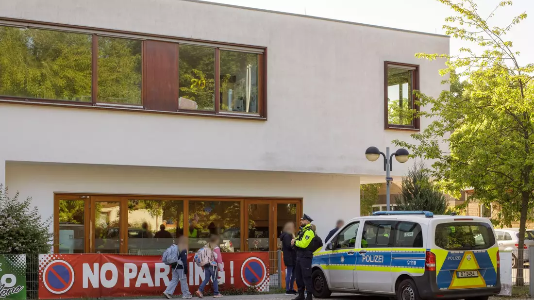 Die Polizei steht vor einer Grundschule im Berliner Bezirk Spandau, während Schüler am Morgen zur Schule kommen.  - Bild: Julius-Christian Schreiner/dpa