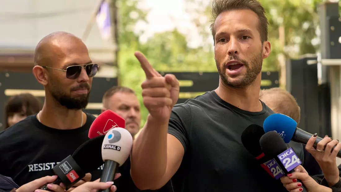 Andrew Tate (links) schaut zu seinem Bruder Tristan Tate, der am 21. Mai vor einer Polizeistation in Voluntari in Rumänien redete. - Bild: Vadim Ghirda/AP/dpa