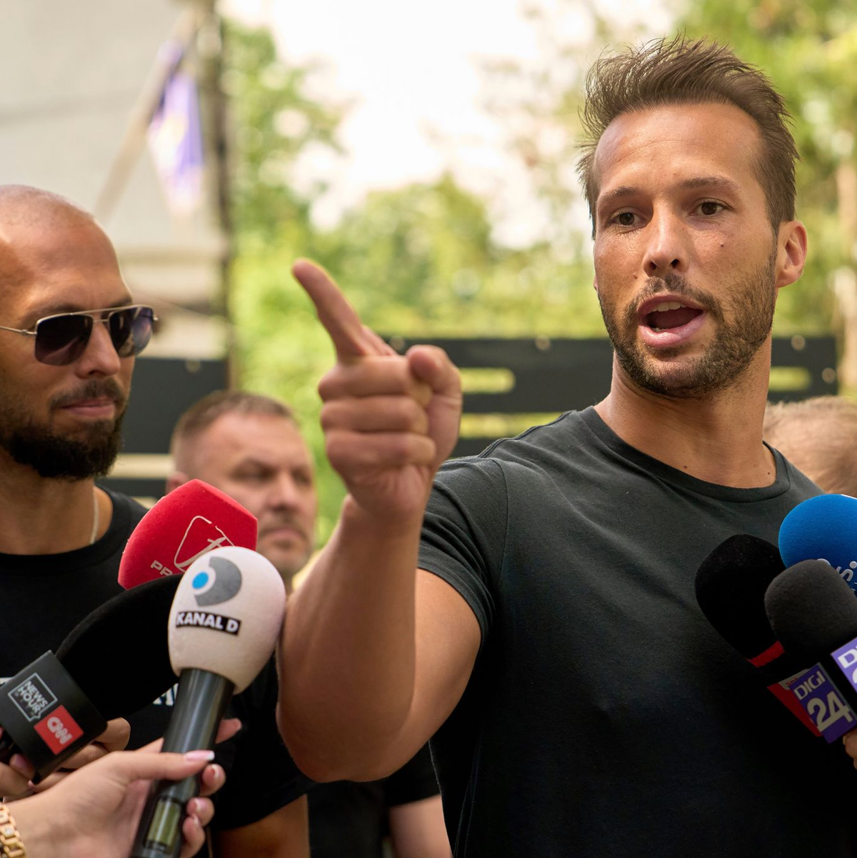 Andrew Tate (links) schaut zu seinem Bruder Tristan Tate, der am 21. Mai vor einer Polizeistation in Voluntari in Rumänien redete. - Foto: Vadim Ghirda/AP/dpa