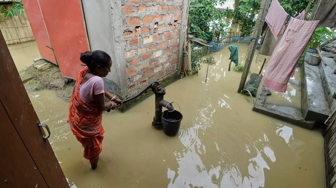 Eine Frau versucht in der überfluteten Umgebung ihres Hauses, Wasser zu sammeln.  - Bild: Uncredited/AP/dpa