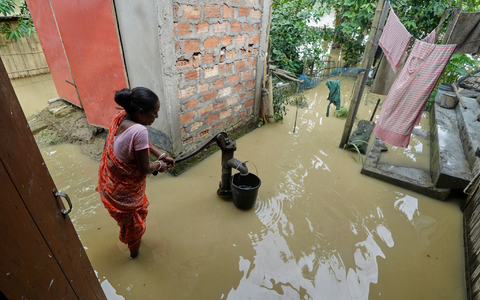 Eine Frau versucht in der überfluteten Umgebung ihres Hauses, Wasser zu sammeln.  - Foto: Uncredited/AP/dpa