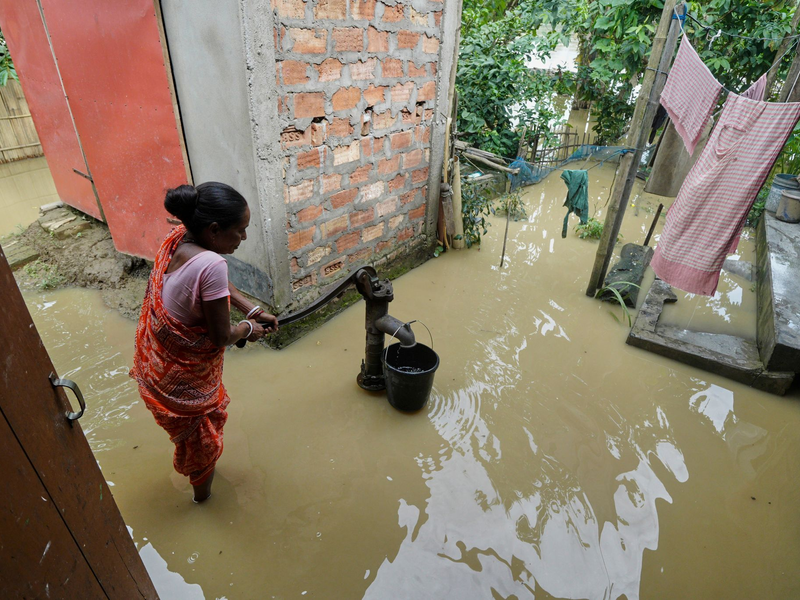 Eine Frau versucht in der überfluteten Umgebung ihres Hauses, Wasser zu sammeln.  - Foto: Uncredited/AP/dpa