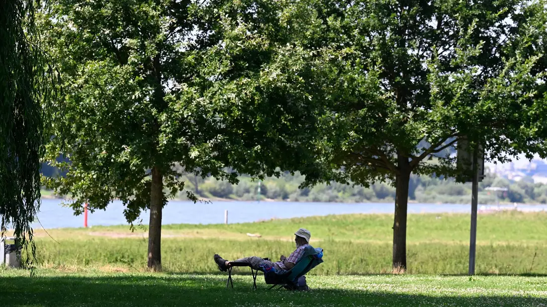 Ein Mann hat sich ein schattiges Plätzchen am Ufer des Rheins in Leverkusen gesucht. (Archivbild) - Bild: Roberto Pfeil/dpa