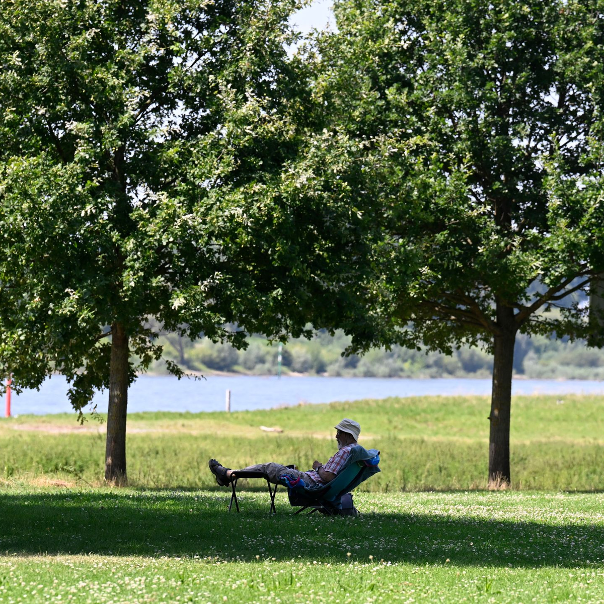 Ein Mann hat sich ein schattiges Plätzchen am Ufer des Rheins in Leverkusen gesucht. (Archivbild) - Foto: Roberto Pfeil/dpa