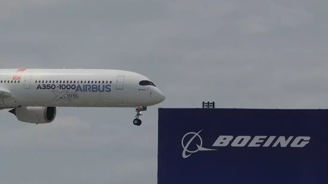 Die zwei großen Konkurrenten: Ein Airbus fliegt bei einer Vorführung auf der Luftfahrtmesse Salon du Bourget an einem Logo von Boeing vorbei. - Bild: Michel Euler/AP/dpa