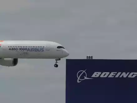 Die zwei großen Konkurrenten: Ein Airbus fliegt bei einer Vorführung auf der Luftfahrtmesse Salon du Bourget an einem Logo von Boeing vorbei. - Foto: Michel Euler/AP/dpa